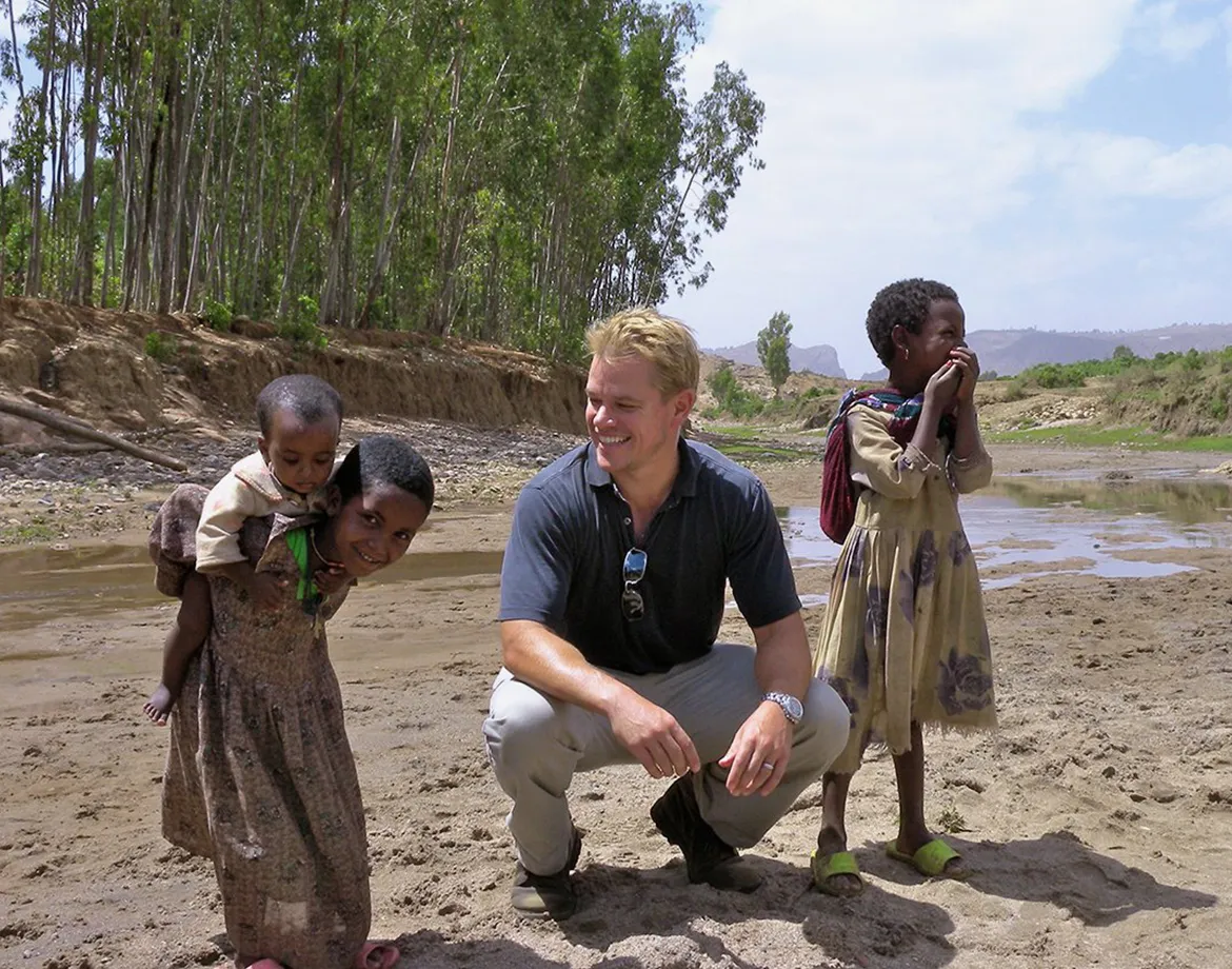 Matt Damon sitting with young children in Africa.