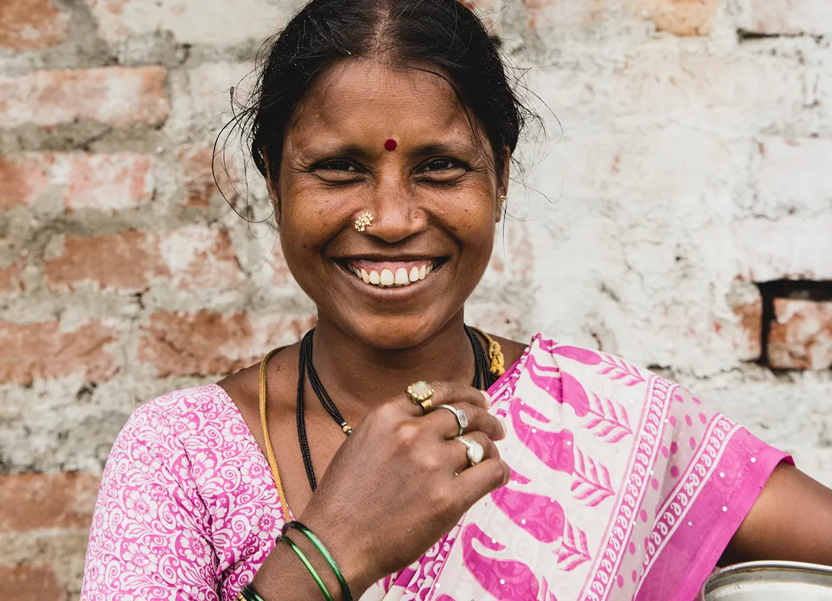 Woman wearing pink sari smiles while holding a water vessel.