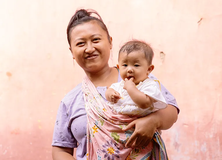 Mother holding her young child in front of a pink wall.