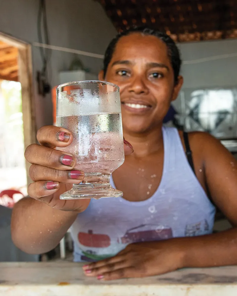 Woman named Erenice smiling while holding a clear glass of safe water.