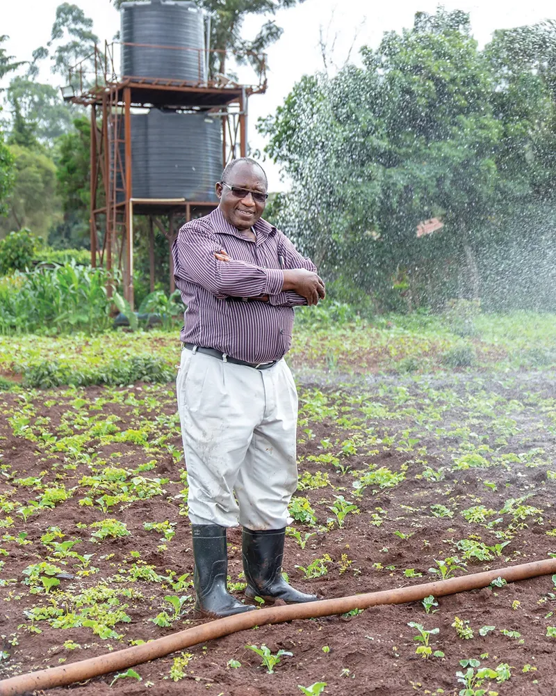 Man standing in front of his crops while they are being watered.