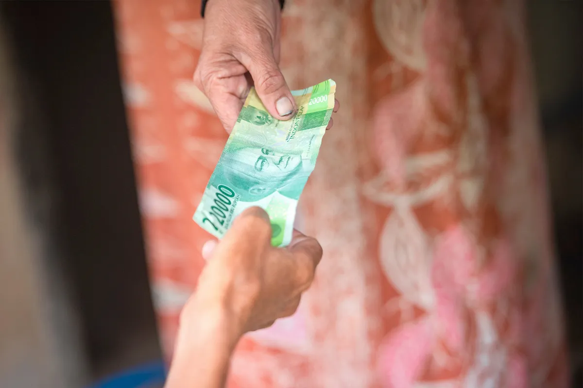 Two hands exchanging a couple of Indonesian Rupiah bank notes.