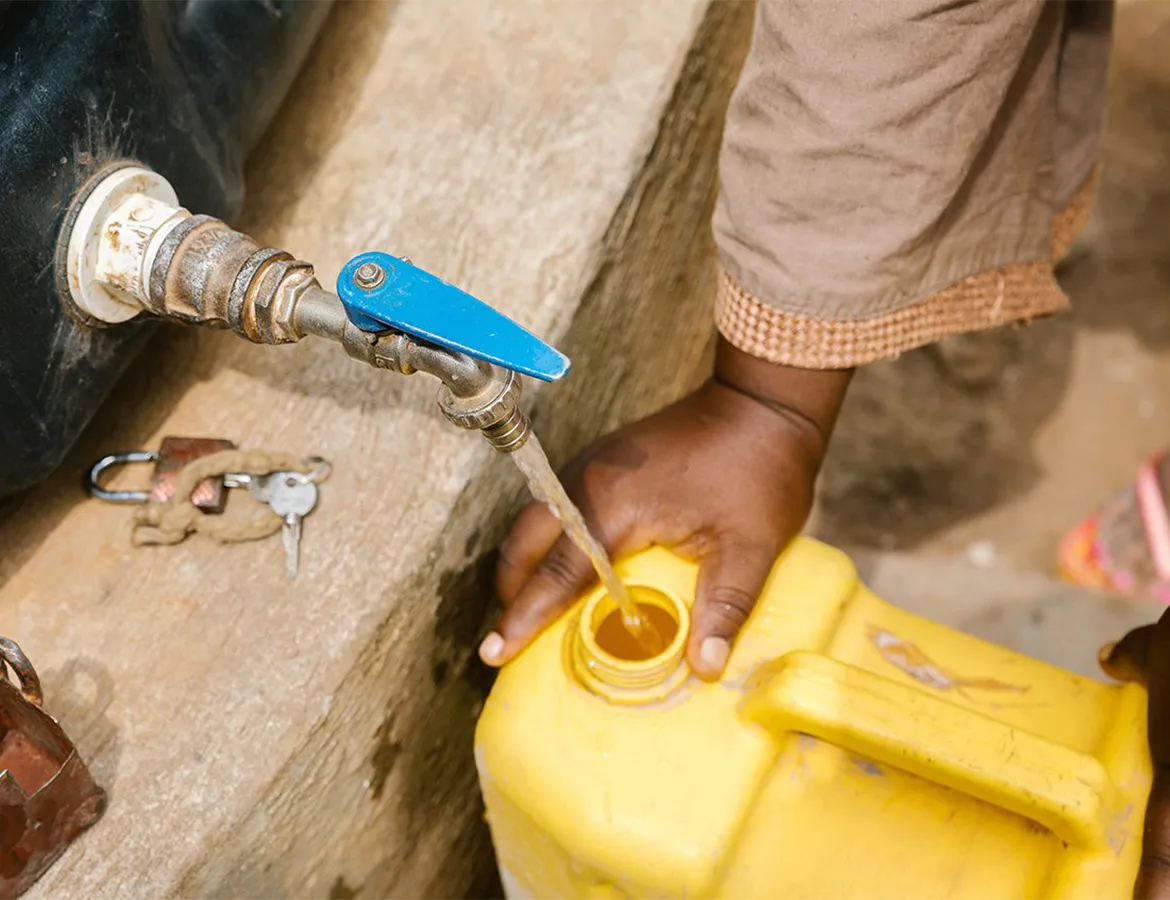 A person filling up a yellow water vessel from a large water tank.