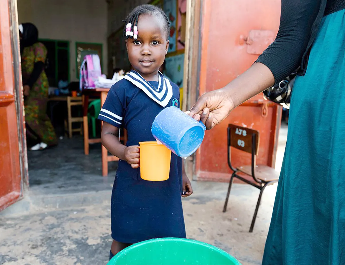 Young girl in a school uniform holding a mug being filled with safe water in Uganda.