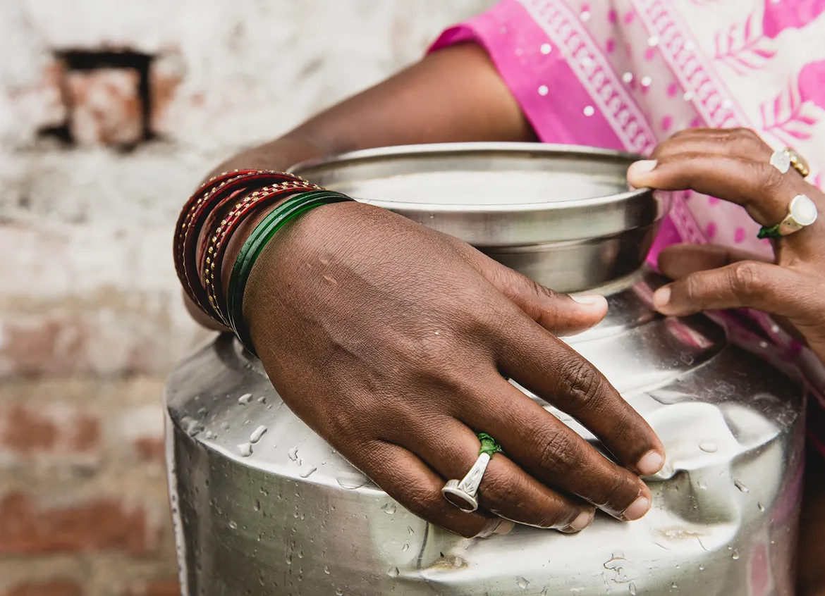 A woman holding a large silver water vessel.