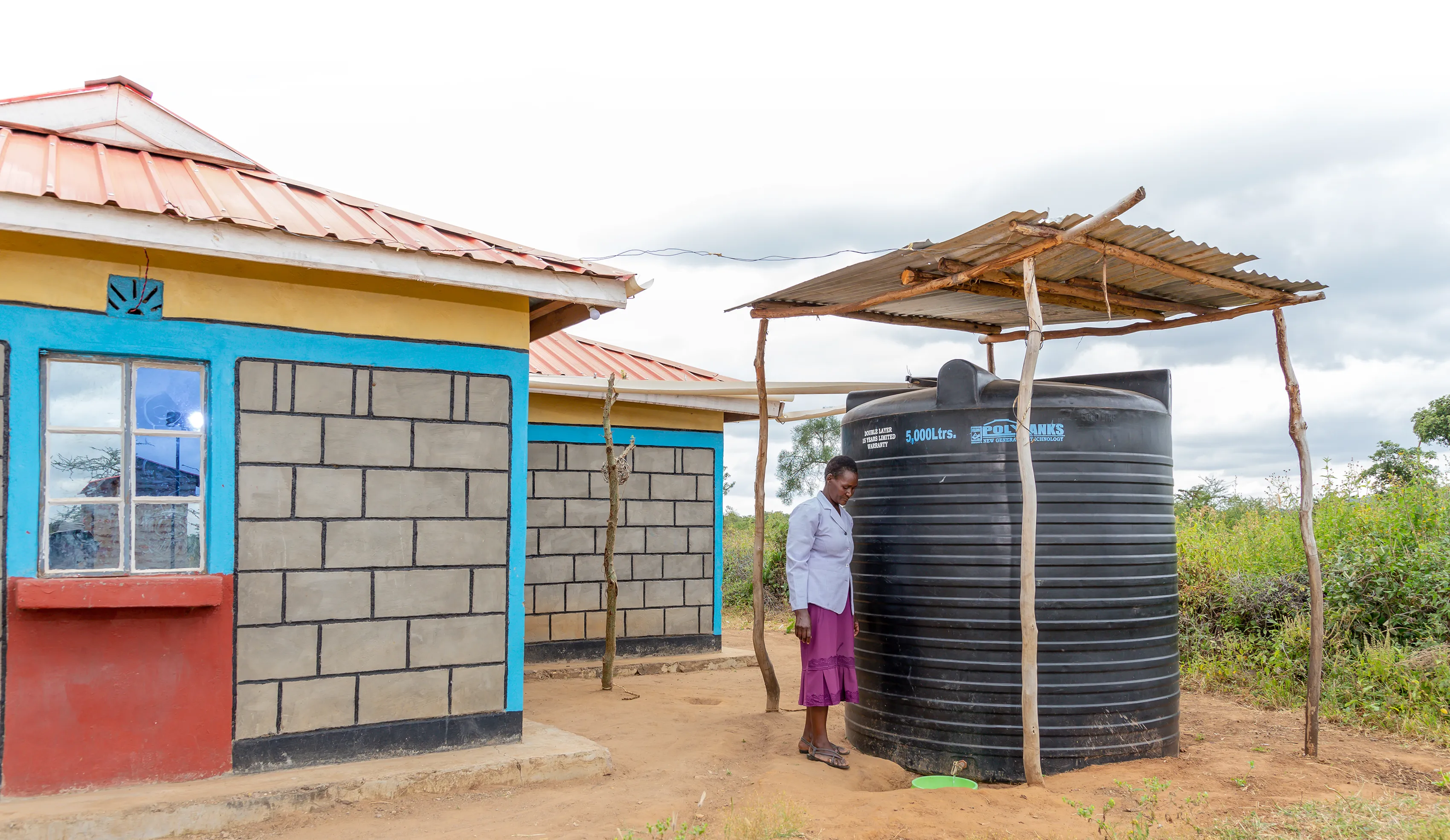 A woman in Kenya standing next to a large rain water catchment tank