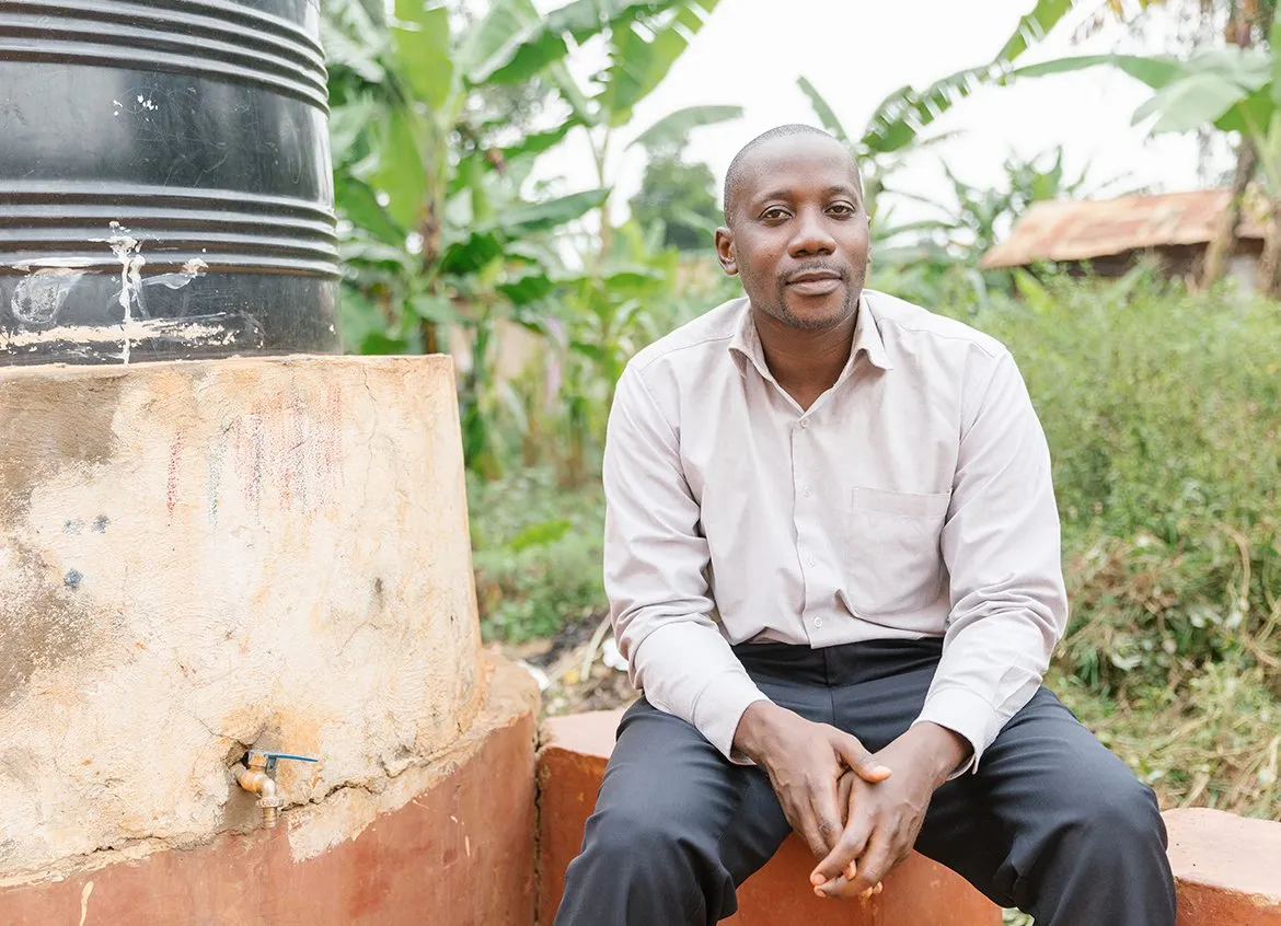 Augustine, a partner from PostBank Uganda sitting next to a tank of safe water.