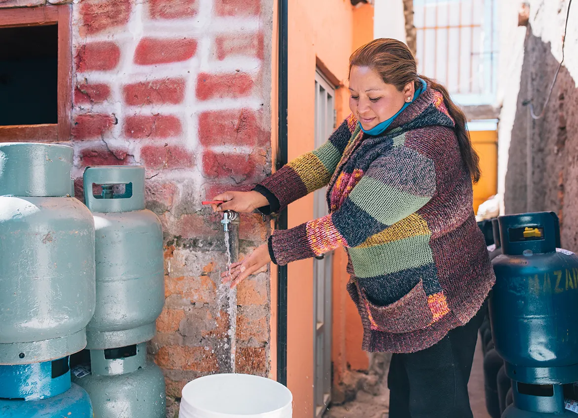 Woman filling up a bucket from a water spout outside her home.