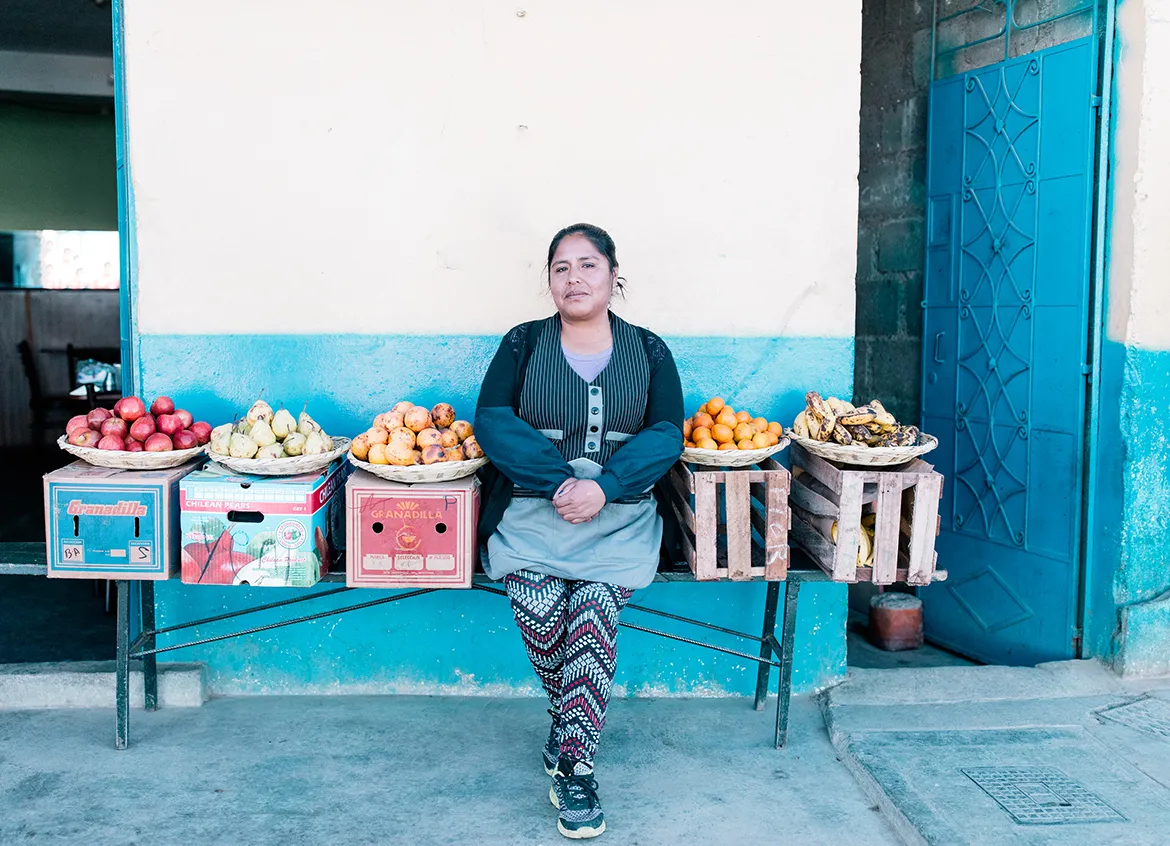 Woman sitting on bench next to fruit that she is selling.