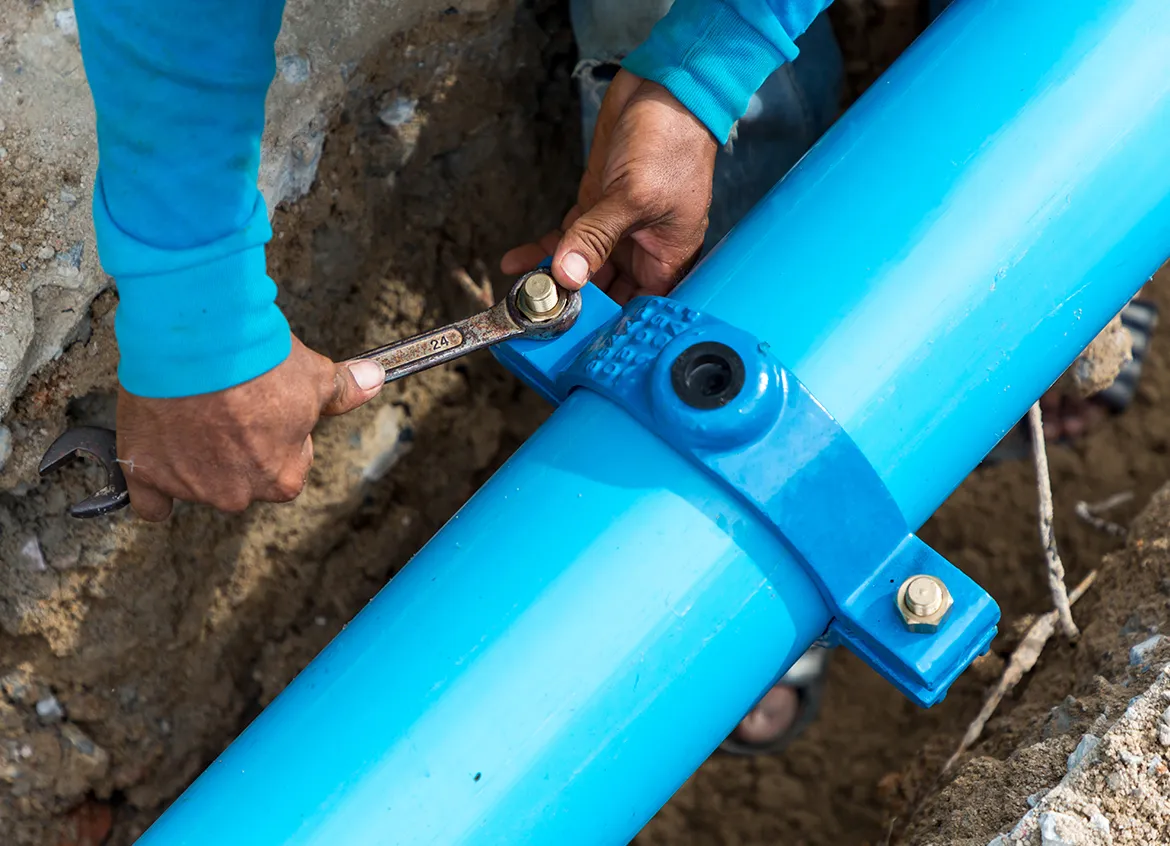 A construction worker uses a wrench to connect a water pipeline.